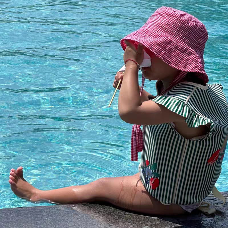 petite fille assise au bord de la piscine avec le gilet de flottaison a rayure vert petit moussaillon