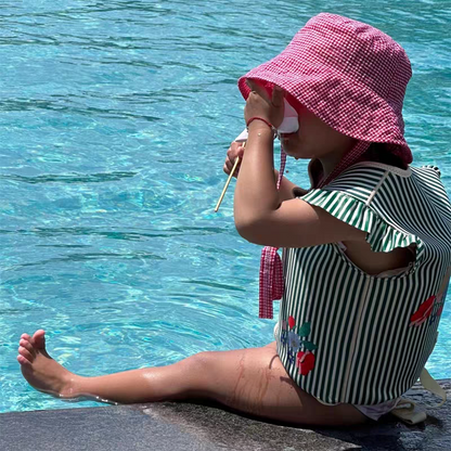 petite fille assise au bord de la piscine avec le gilet de flottaison a rayure vert petit moussaillon